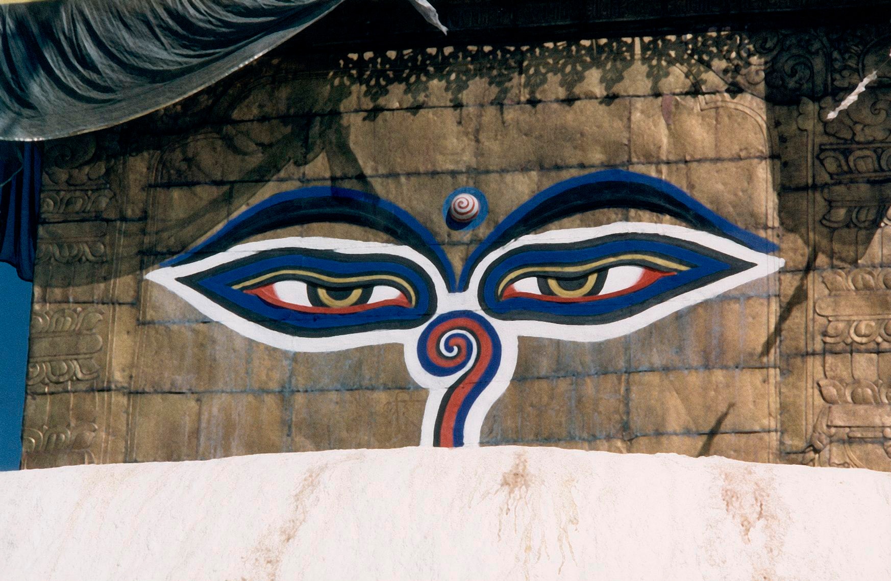 The all-seeing Buddha eyes painted in blue, gold, and red on the stone face of a stupa in Kathmandu