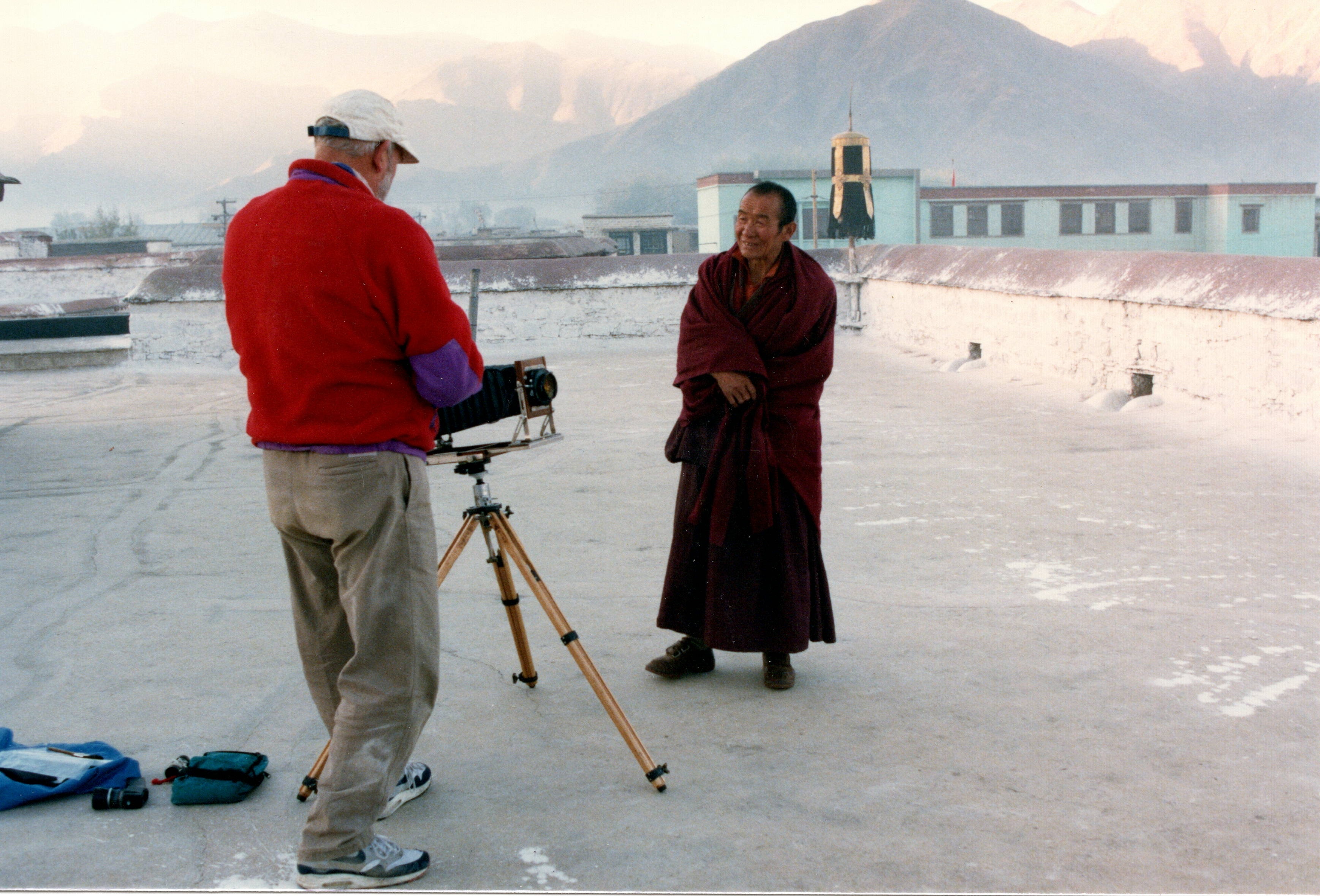 Jack photographing a smiling monk on the roof of the Jokhang Temple, Lhasa, mountains behind