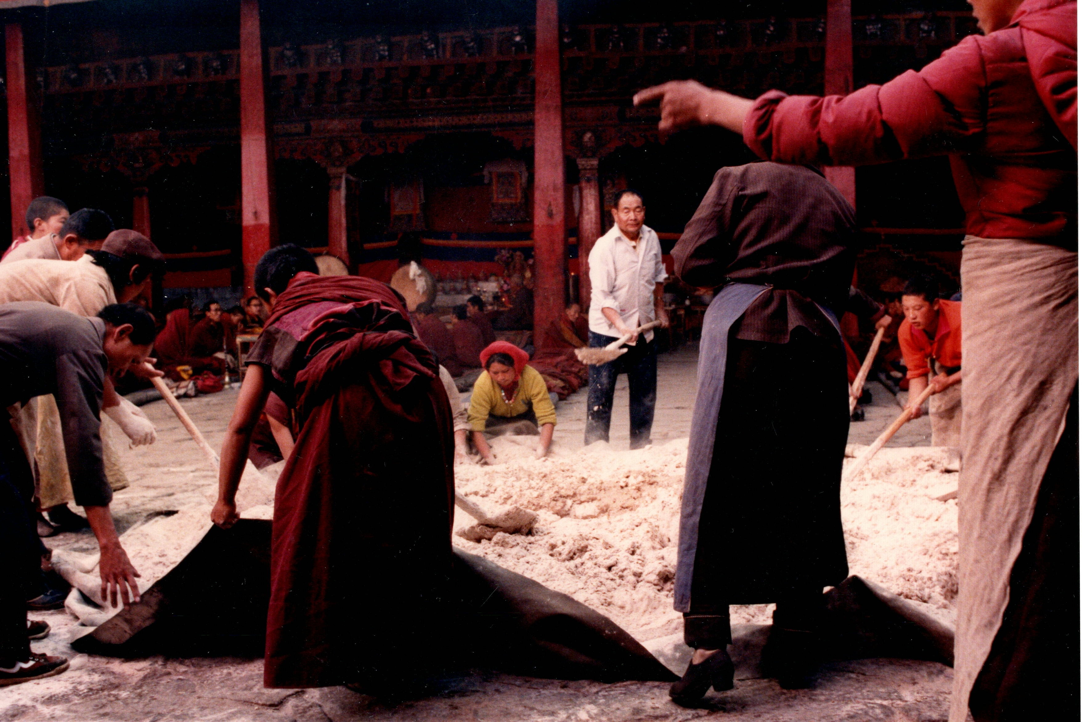 Monks and laypeople working barley flour into tsampa on large tarps in the Jokhang Temple