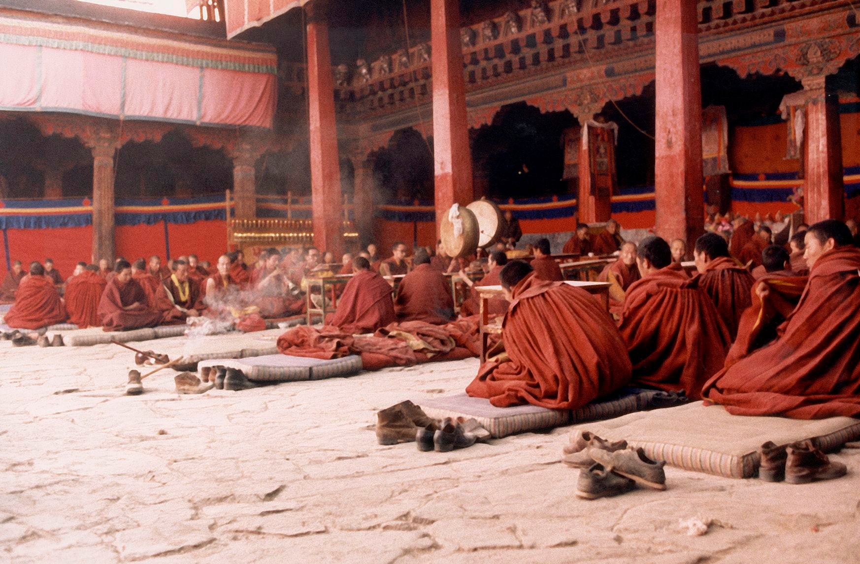Monks seated in rows chanting sutras in the Jokhang Temple main hall, incense smoke rising